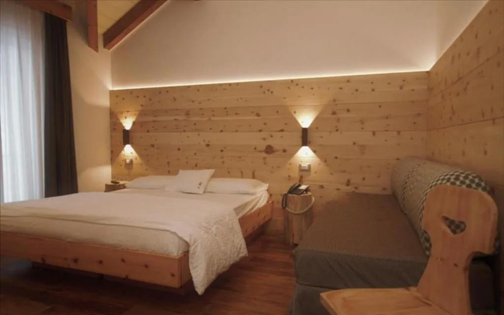 Camera in stile alpino con letto in legno di cirmolo, divano e illuminazione soffusa