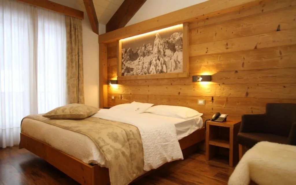 Camera elegante con letto in legno, quadro delle Dolomiti e ampia finestra luminosa