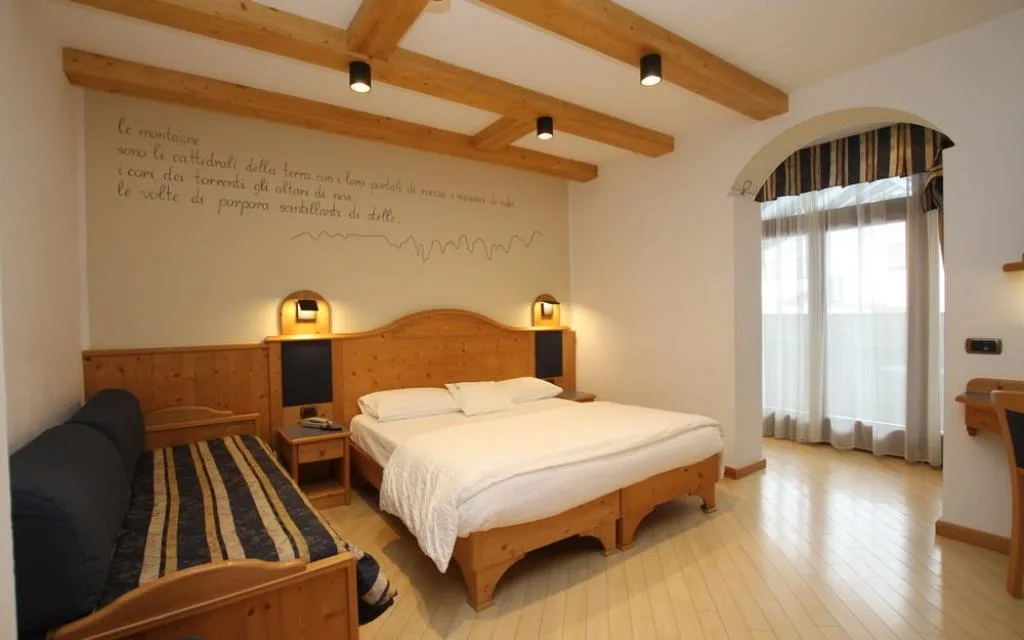 Camera con letto matrimoniale, divano, travi a vista e scritta poetica sulla parete