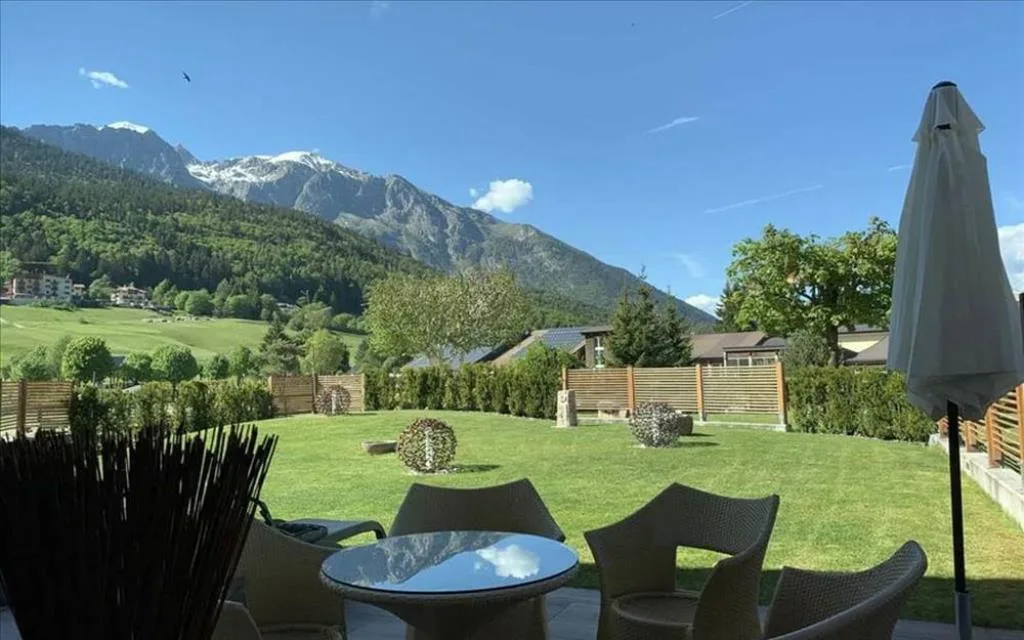 Terrazza con tavolo e sedie in vimini affacciata sul giardino verde e le montagne innevate
