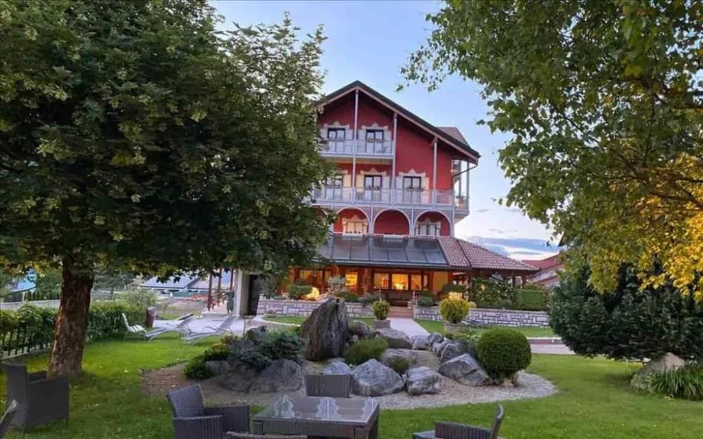 Facciata rossa dell'hotel immersa nel verde con giardino roccioso e alberi in estate