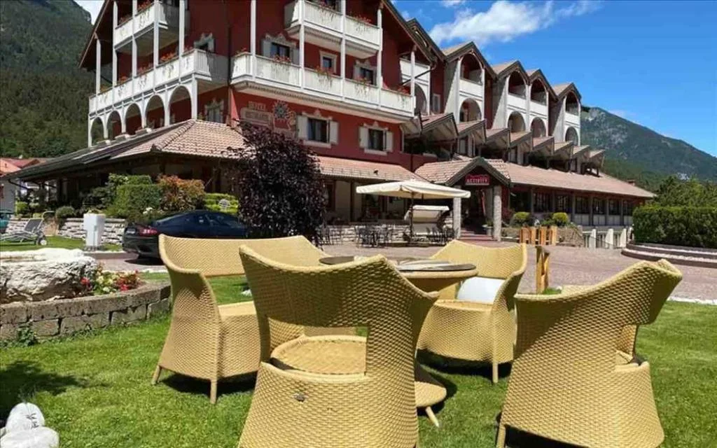 Esterno dell'hotel con tavoli e poltrone in vimini sul prato e montagne sullo sfondo