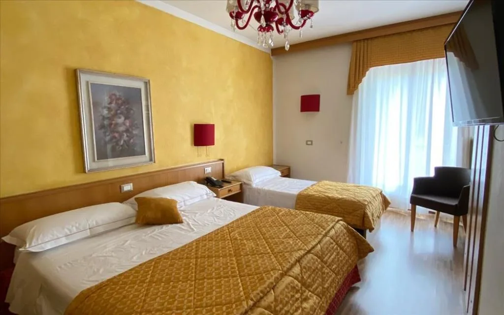 Camera con letto matrimoniale e singolo, pareti gialle, lampadario e TV a parete