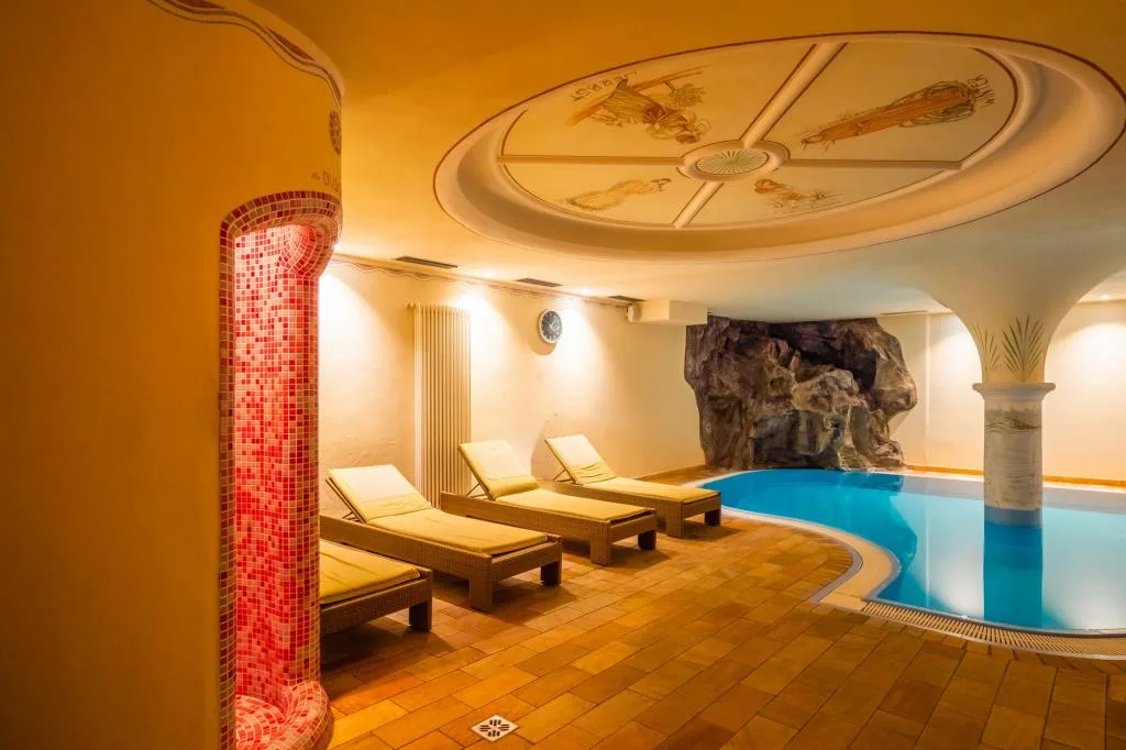 Piscina coperta con grotta rocciosa, lettini e soffitto affrescato