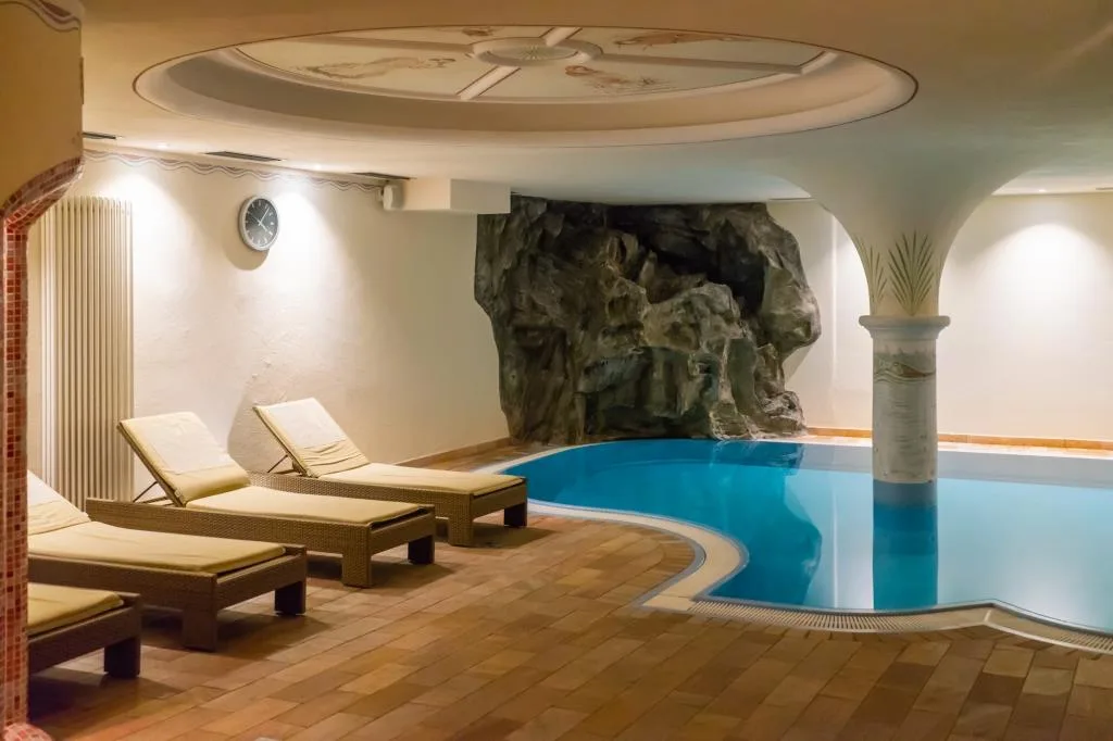Piscina interna con grotta artificiale, colonna decorata e lettini relax
