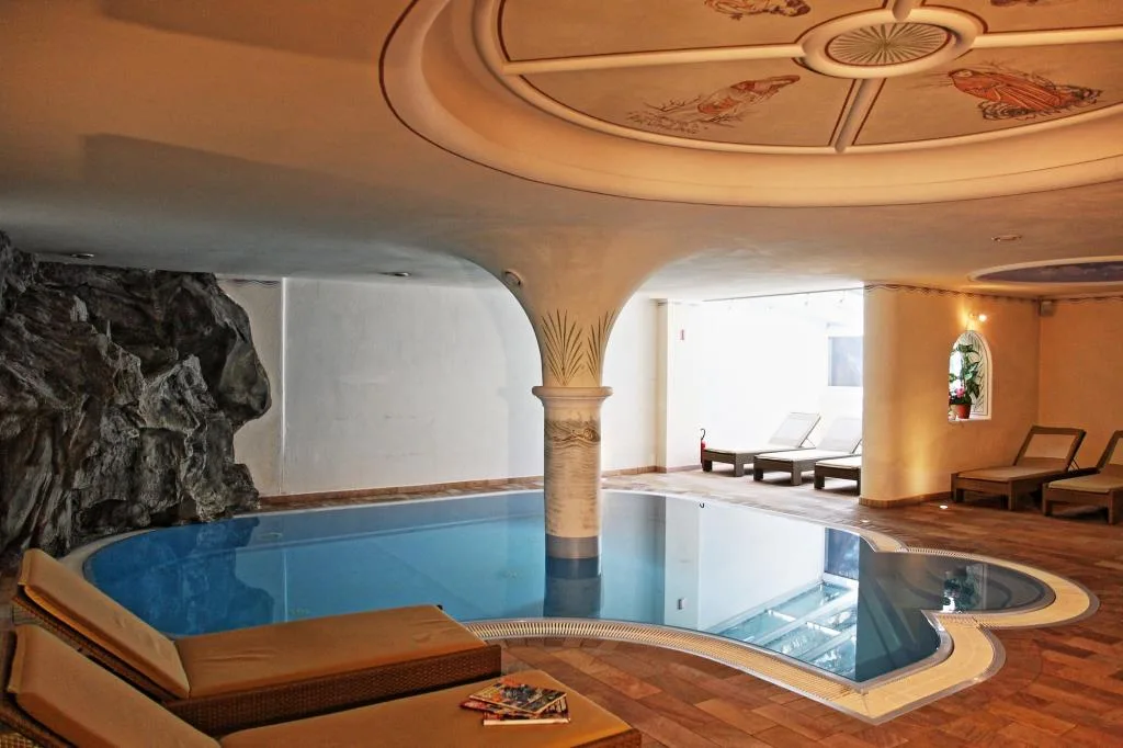 Piscina coperta con colonna centrale, grotta rocciosa e soffitto affrescato