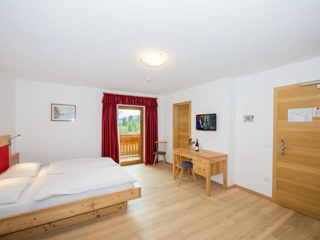 Camera spaziosa con letto in legno, scrivania e balcone con tende rosse