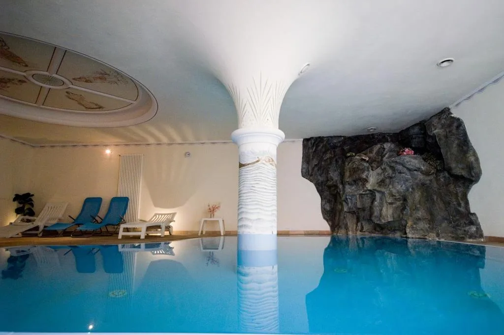 Piscina coperta con colonna bianca decorata e parete rocciosa