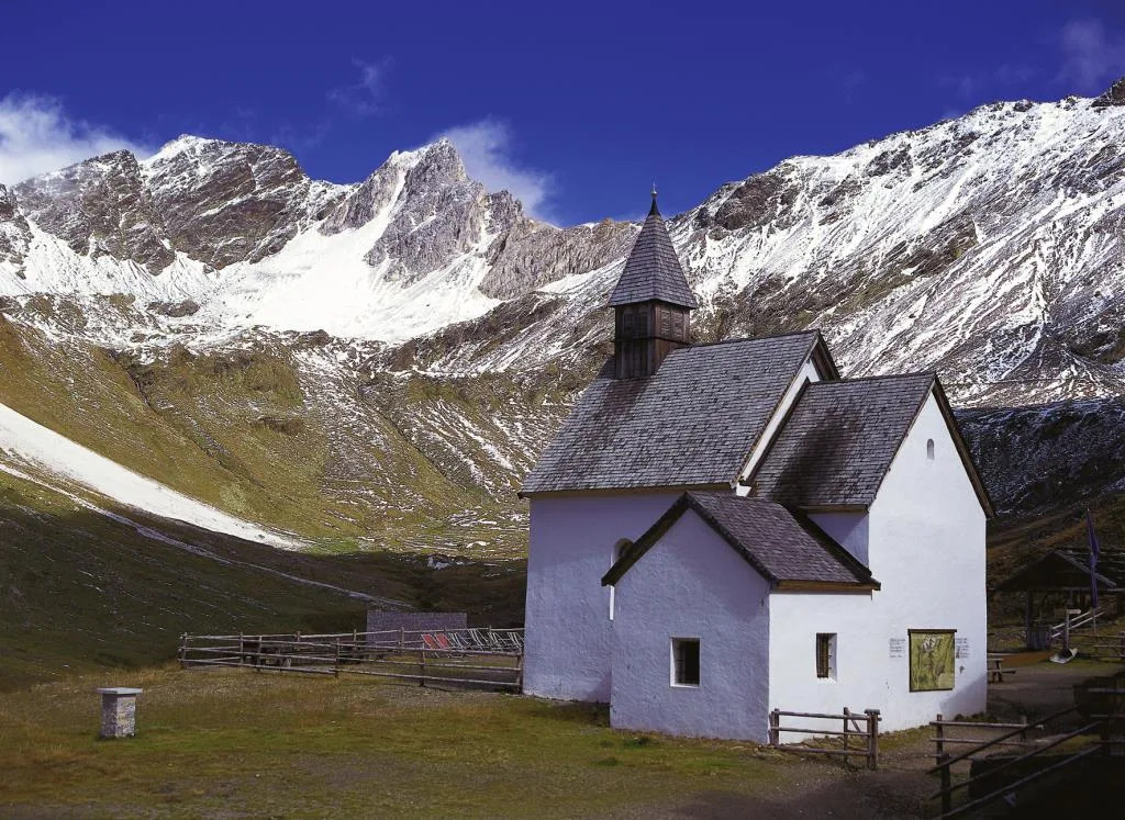Piccola chiesa bianca ai piedi di montagne innevate in alta quota