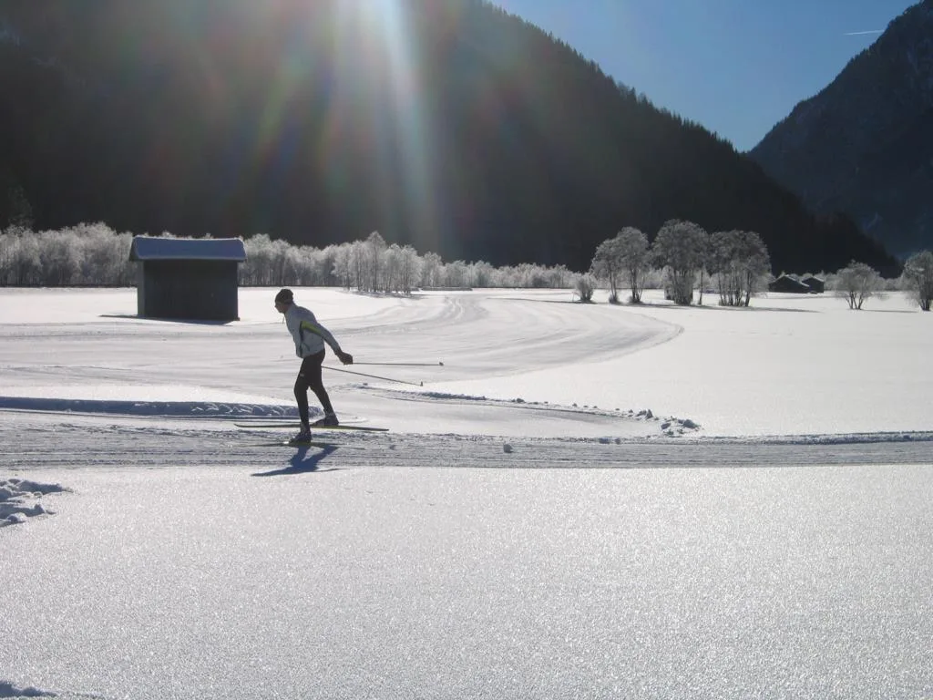 Sciatore di fondo su pista innevata in una valle soleggiata tra le montagne