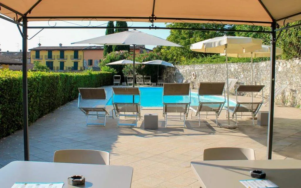Piscina vista da un gazebo con lettini, ombrelloni e terrazza pavimentata