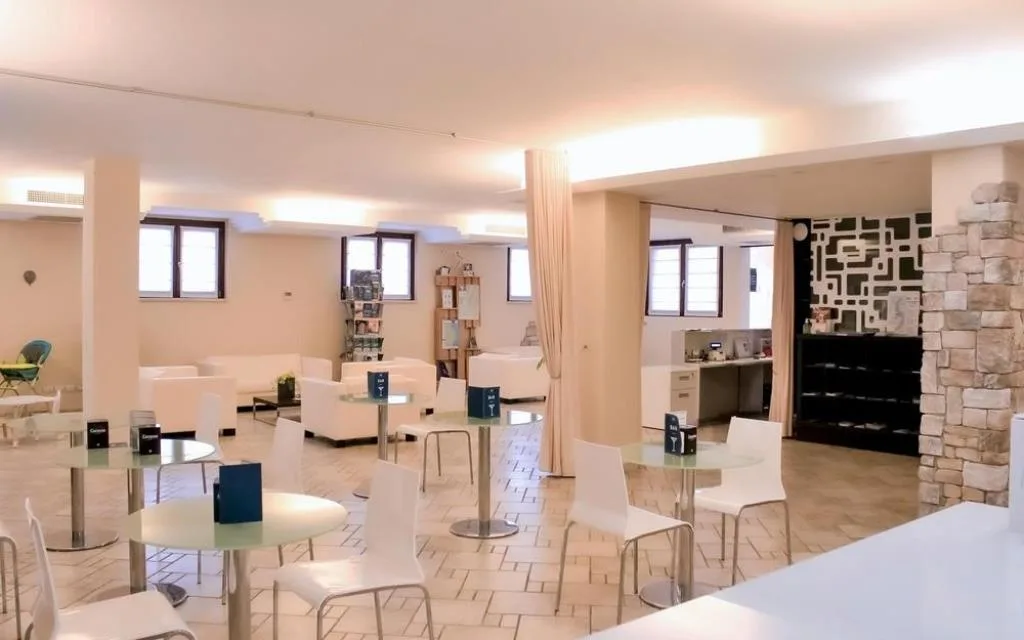Sala bar interna con tavolini, sedie bianche e parete in pietra decorativa
