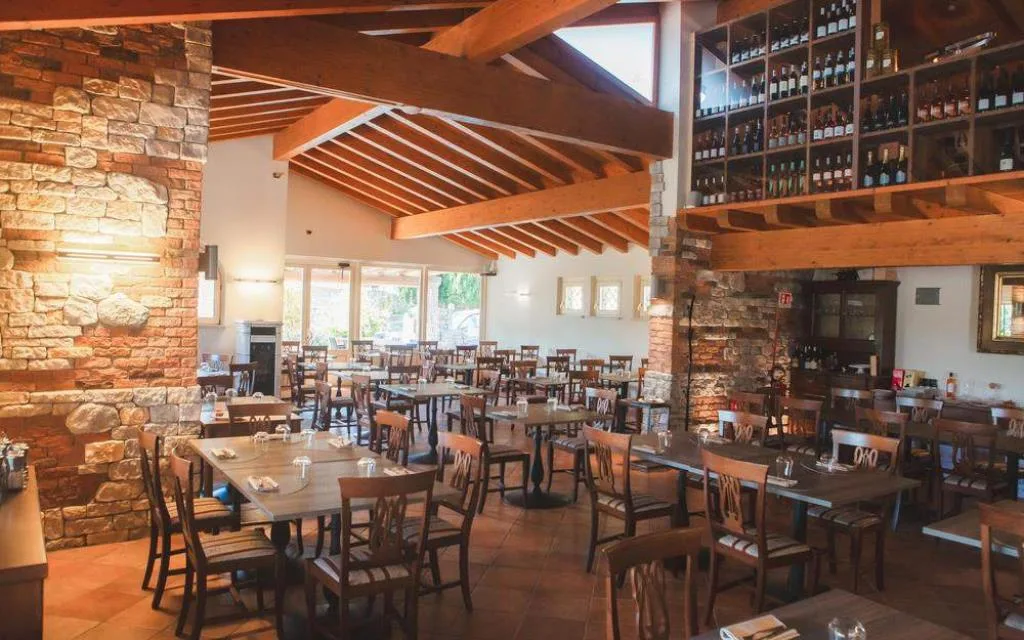 Sala ristorante interna con travi in legno, pareti in pietra e tavoli apparecchiati
