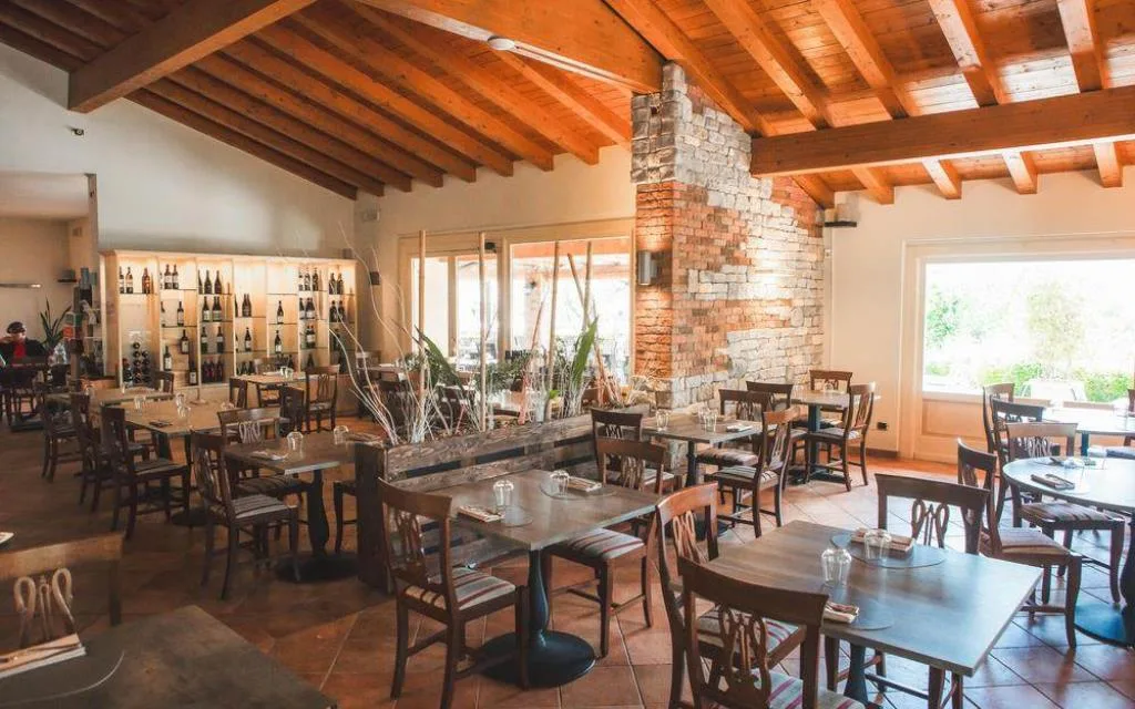 Interno del ristorante con soffitto in legno, parete in mattoni e tavoli apparecchiati