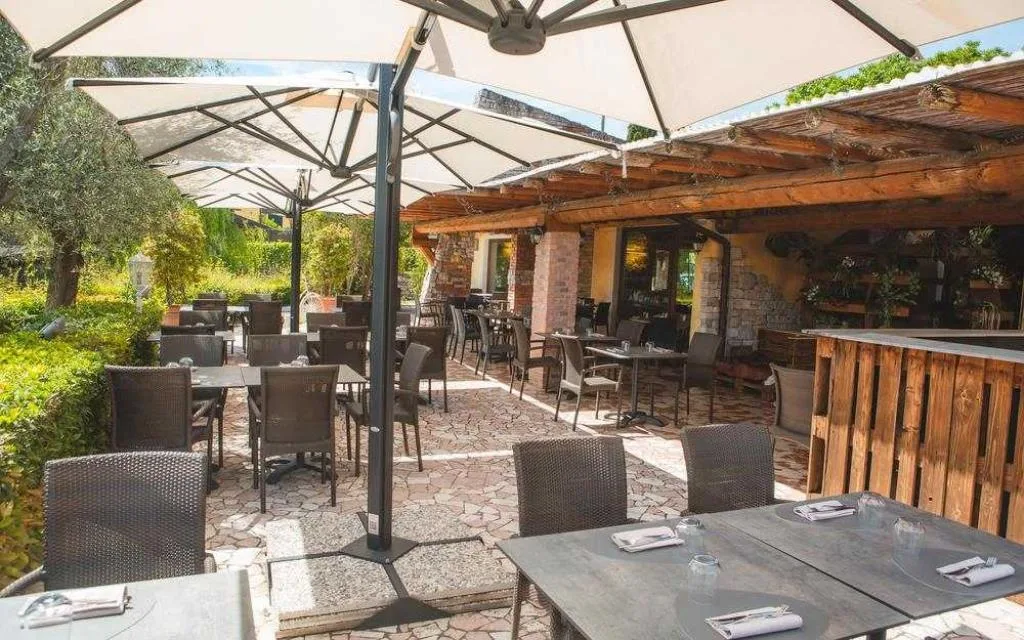 Terrazza ristorante all'aperto con ombrelloni, tavoli e giardino circostante