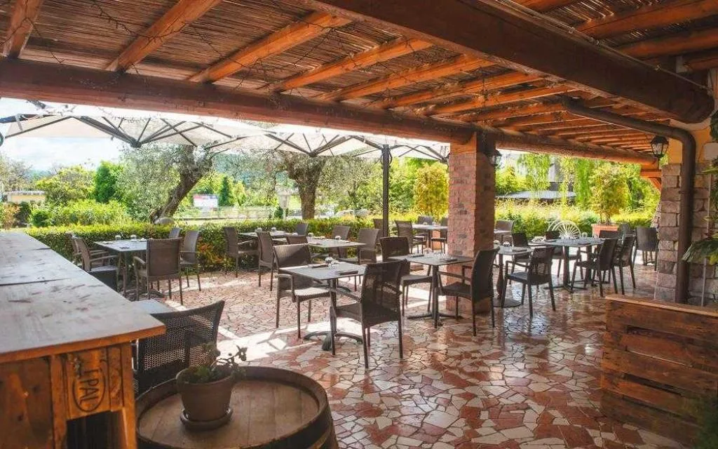 Area pranzo esterna sotto pergolato in legno con tavoli e vista sul giardino