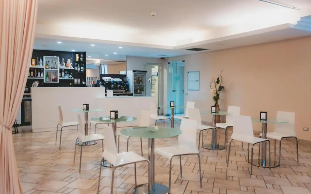 Sala colazione e bar con tavolini rotondi, sedie bianche e bancone