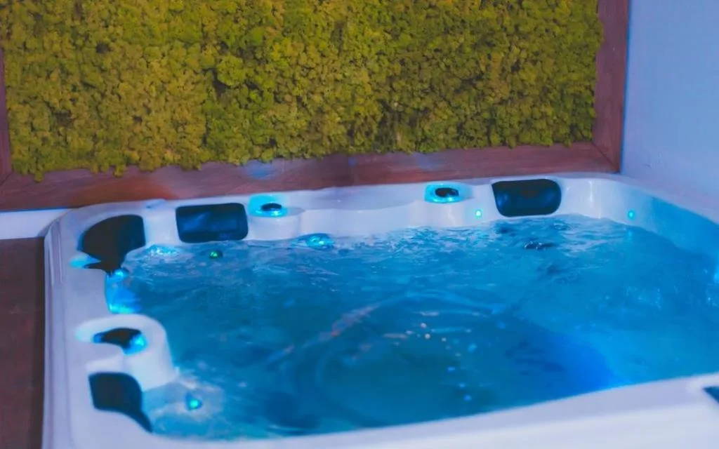 Vasca idromassaggio con acqua illuminata di blu e parete di muschio verde