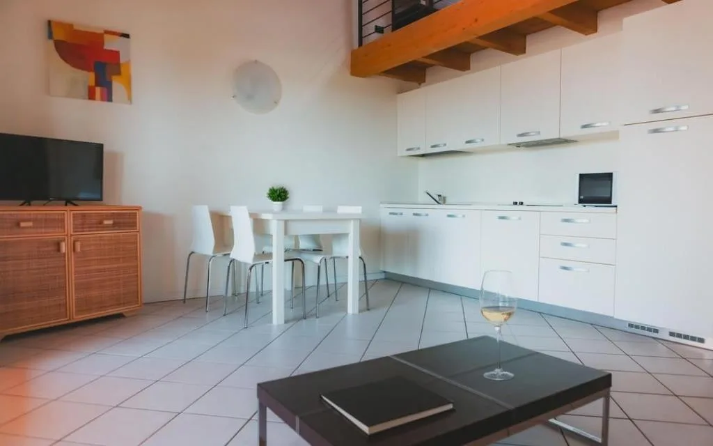 Zona living con angolo cottura, tavolo da pranzo e soppalco in legno