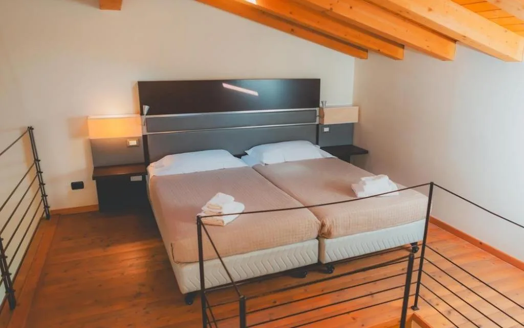Camera mansardata con letto matrimoniale, travi in legno e pavimento in parquet