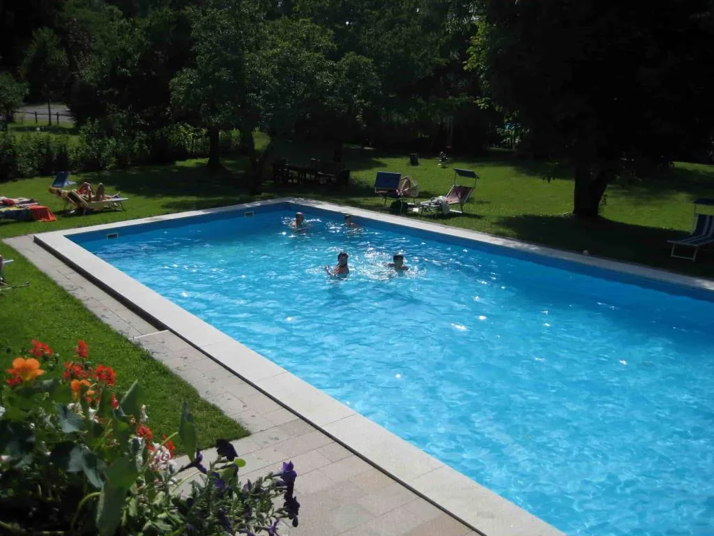 Piscina esterna con ospiti in giardino alberato dell'hotel