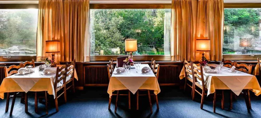 Sala ristorante con tavoli apparecchiati e ampie finestre sul giardino