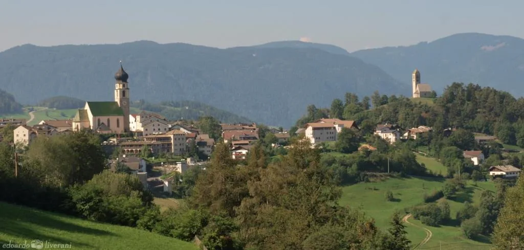 Panorama del villaggio alpino con chiesa e colline verdi